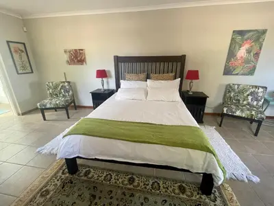 a bedroom with a large bed with two chairs at Lakeview Cottage: Rural Retreat in Pampoenkraal