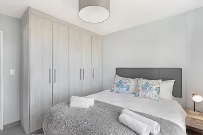 a white bedroom with a large bed and a cabinet at Ocean View 503 in Bloubergstrand