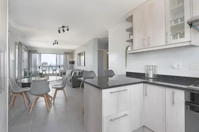 a kitchen with white cabinets and a table and chairs at Ocean View 503 in Bloubergstrand