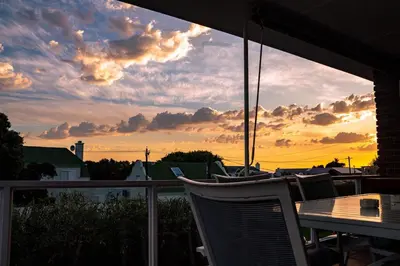 a table and chairs on a balcony with a sunset at The Mountainview Family Retreat in Hermanus