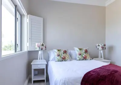 a white bedroom with a bed with pillows and a window at Seafront Retreat in Sandbaai in Hermanus