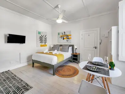 a white bedroom with a bed and a table at Obs Loft Apartments Observatory in Cape Town