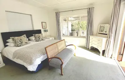 a bedroom with a bed and a chair and a window at Grotto Cottage in Hermanus