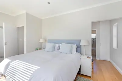 a white bedroom with a large white bed with blue pillows at Sunset Villa 50 in Cape Town