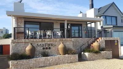 a house with tables and chairs on the balcony at Mafari Beach House in Hermanus