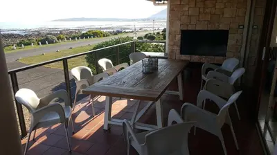 a wooden table and chairs on a balcony with a television at Mafari Beach House in Hermanus