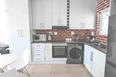 a kitchen with white cabinets and a brick wall at 6 Culemborg Court, 5 Culemborg Street, Strand, Cape Town in Cape Town