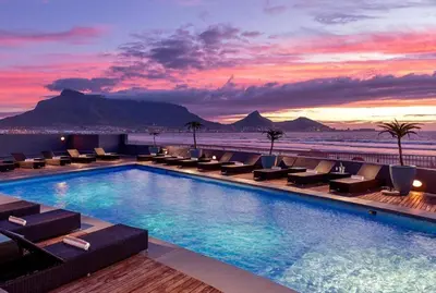 a hotel pool with chairs and a sunset at Luxury Beach Escape Sleeps 4 - Ocean View - Spa - Pool - Gym - Back Up Power in Cape Town