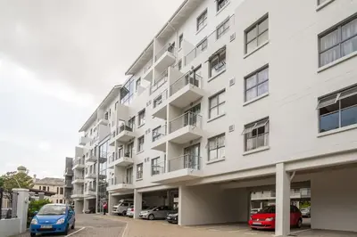 a white building with cars parked in a parking lot at Rondebosch Central in Cape Town