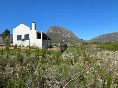 a white house in a field with mountains in the background at Sneeukop Mountain Cottage in Paarl