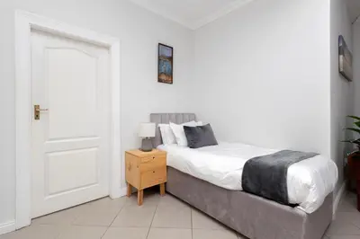 a white bedroom with a bed and a night stand at SERENA INN Apartment no5 in Cape Town