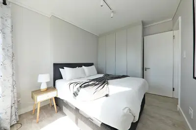 a bedroom with a large white bed and a table at 002 Burmeister on Park- 2 minute walk from the beach in Cape Town