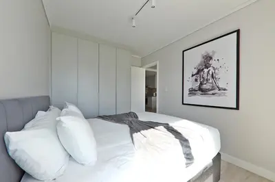 a bedroom with a bed with white pillows and a painting at 002 Burmeister on Park- 2 minute walk from the beach in Cape Town
