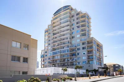 a tall apartment building with palm trees in front of it at Stylish Sunlit Ocean View Oasis! in Cape Town