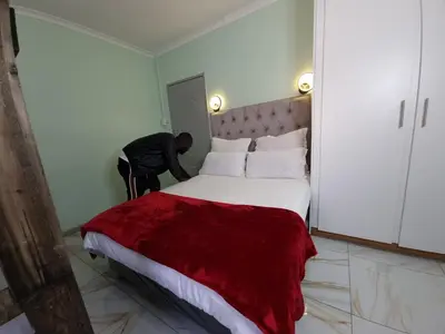 a man standing next to a bed in a room at Ojong's Guesthouse Kraaifontein - Eikendel in Cape Town