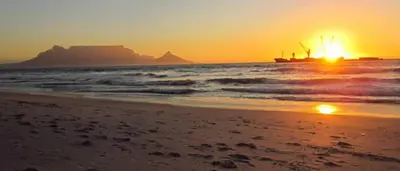 a sunset on the beach with a ship in the ocean at The Great escape 5 mins away from Blouberg Beach in Cape Town