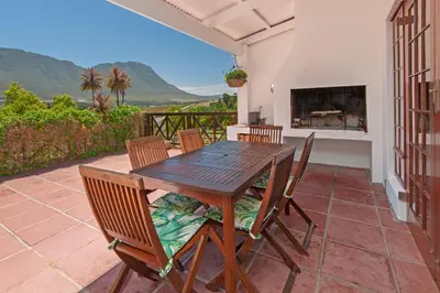 a wooden table and chairs on a patio with a fireplace at High Season Farm Luxury Cottages in Hermanus