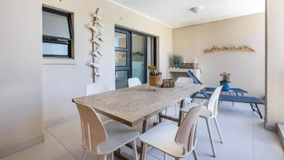 a dining room with a wooden table and white chairs at The W-Collection Esplanade Hermanus in Hermanus