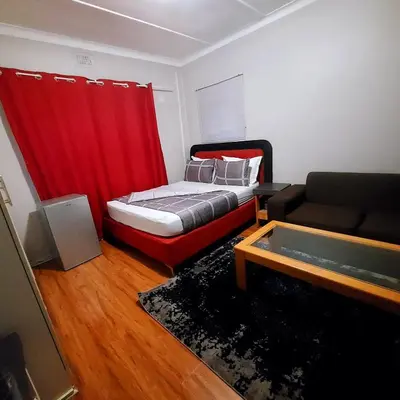 a bedroom with a bed with a red curtain and a couch at GALAXY BOSTON BELLVILLE in Cape Town