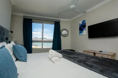 a bedroom with a large white bed with a flat screen tv at Ocean Breeze Hotel in Strand