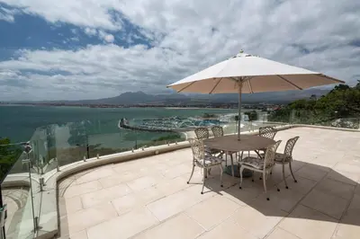 a table and chairs with an umbrella on a balcony at 'Harbour Views' - 2 bedroom, sleeps 4 with private pool and large veranda! in Gordonʼs Bay