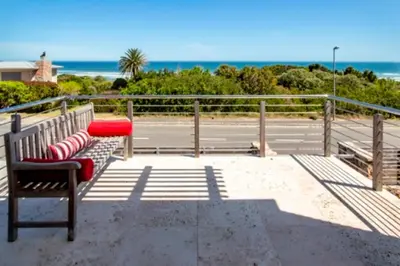 a bench with red pillows sitting on a beach at Grandeur in Hermanus