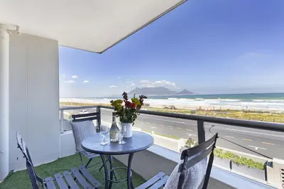 a table and chairs on a balcony with a view of the beach at Sea Spray B104 in Table View