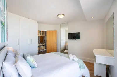 a bedroom with a white bed with a tv on the wall at Beachfront Luxury Apartment - Hibernian Towers 309 Strand - Self Catering in Cape Town