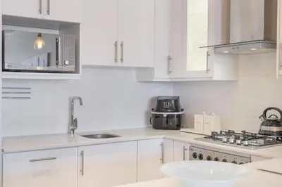 a white kitchen with a sink and a microwave at Portico 704 in Bloubergstrand