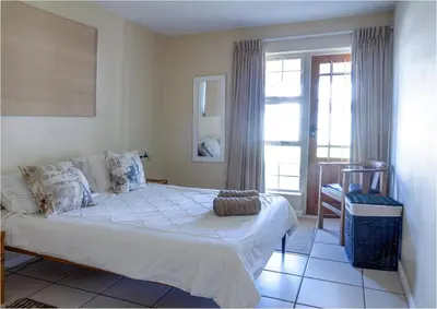 a bedroom with a bed and a chair and a window at Sunset Terrace in Hermanus