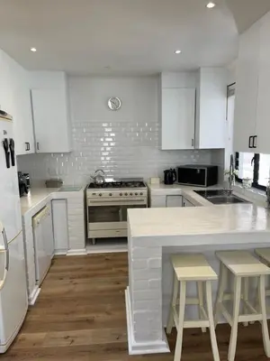 a kitchen with white cabinets and a kitchen island with stools at Fynbos Feniks Family House in Voëlklip in Hermanus