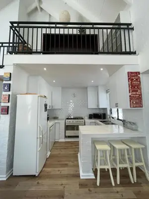 a kitchen with a white refrigerator and some stools at Fynbos Feniks Family House in Voëlklip in Hermanus