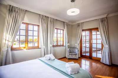 a bedroom with a bed and a chair and windows at Villa Luisa: Sun-filled hidden gem with Pool. in Cape Town