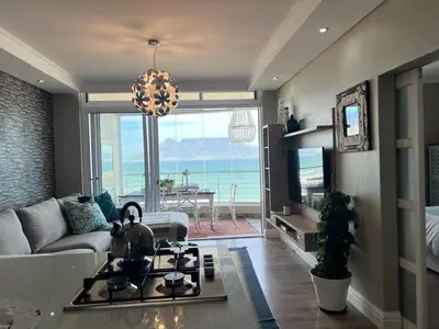 a living room with a couch and a kitchen with a view of the ocean at Portico 705 in Cape Town