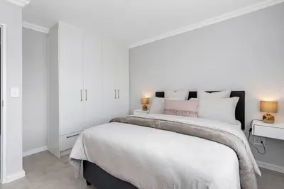 a bedroom with a large bed with white walls at Elegant, Spotless 2 Bed For Enchanted Stays in Cape Town