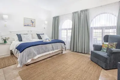 a white bedroom with a bed and a chair at Casa Familia in Hermanus