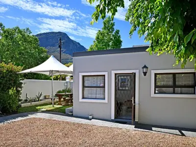a gray house with a table and an umbrella at La Rochelle Cottage in Franschhoek