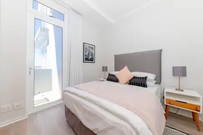 a white bedroom with a large bed and a window at Horizon Bay 1603 by HMH in Cape Town