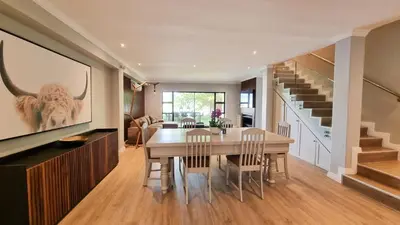 a dining room with a table and a tv and stairs at Pearl Valley Golf Lodge - loadshedding free in Simondium