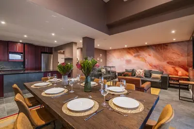 a dining room and living room with a table and chairs at Serviced Beach Penthouse, 100k Gemstone display, All Ensuite in Cape Town