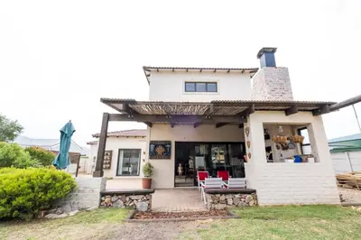 a white house with red chairs on the porch at La Haven Self Catering in Hermanus