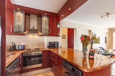 a kitchen with wooden cabinets and a counter top at Beachfront 3rd floor 2 bedroom w communal swimming pool- B16 Blouberg in Bloubergstrand