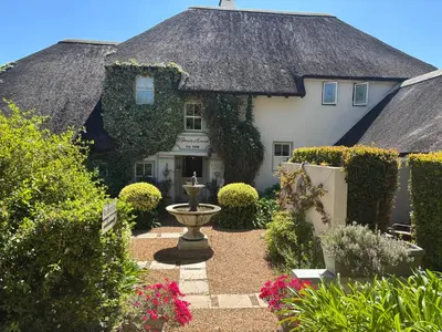 a house with a thatched roof and a garden at In the Vine Country Manor Guesthouse in Stellenbosch