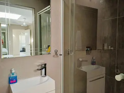 a bathroom with a sink and a shower with a mirror at 'Antilles'- 6 Bedroom Luxury Villa On The Beach, Sleeps 12 in Gordonʼs Bay