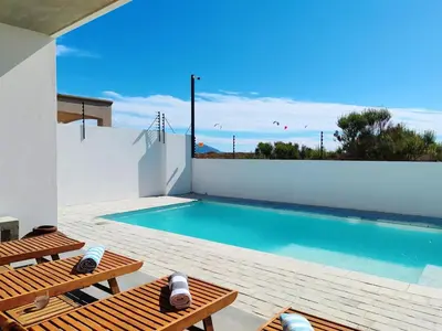 a swimming pool with two wooden benches next to a house at Drift Sunset Beach House in Sunset Beach