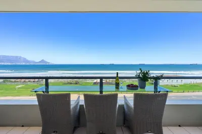 a table with chairs and a view of the ocean at Sea Spray B306 in Bloubergstrand