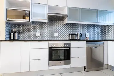 a white kitchen with white cabinets and appliances at Sea Spray A308 in Bloubergstrand