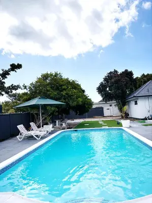 a large blue swimming pool with an umbrella and chairs at Urban Cosy City Haven in Cape Town