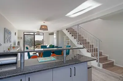 a kitchen with a staircase and a living room at Resort Style Penthouse - BackUp Power in Cape Town