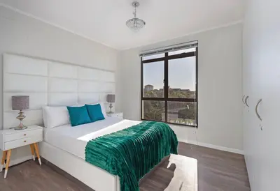 a white bedroom with a large bed and a window at Resort Style Penthouse - BackUp Power in Cape Town